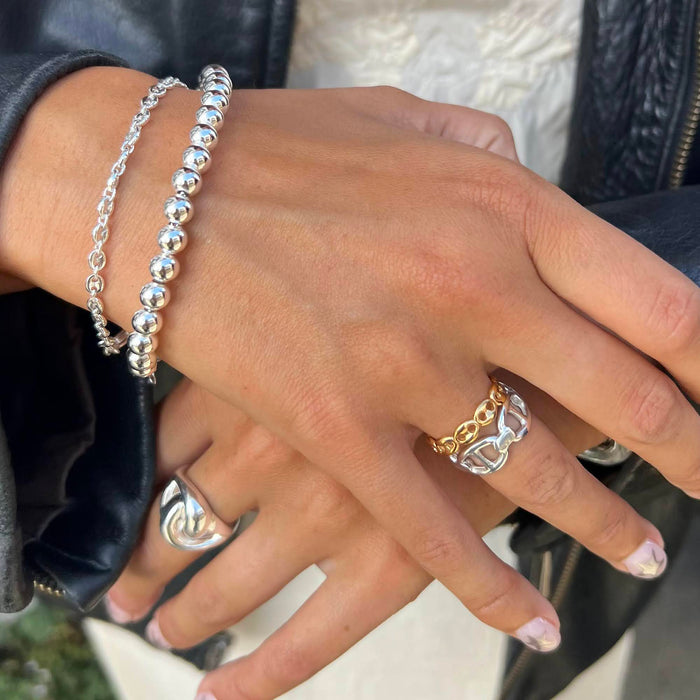 Close-up of a hand wearing silver bracelets and rings with a blurred background - seol gold