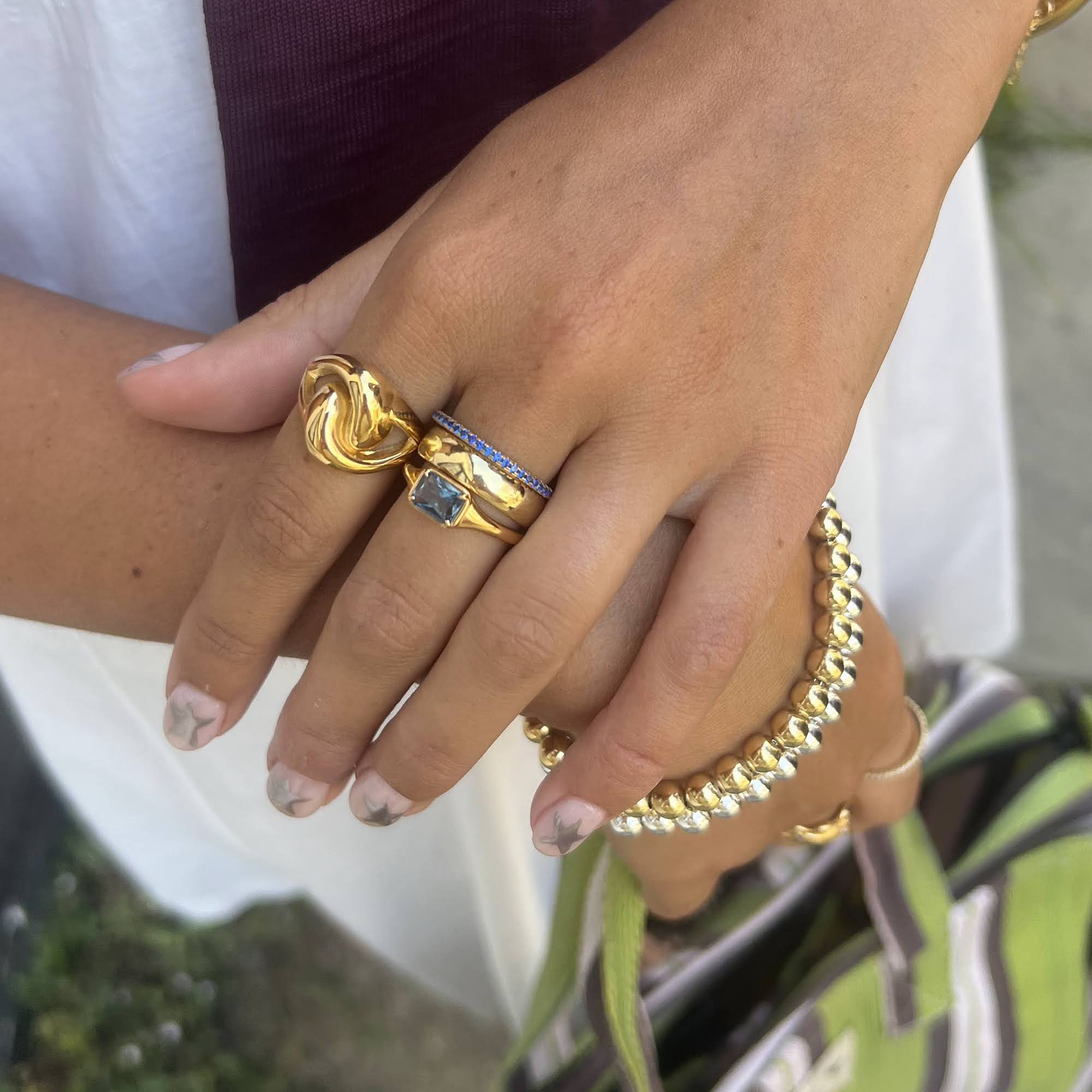 Close-up of a hand wearing multiple gold rings with a blurred background - seolgold
