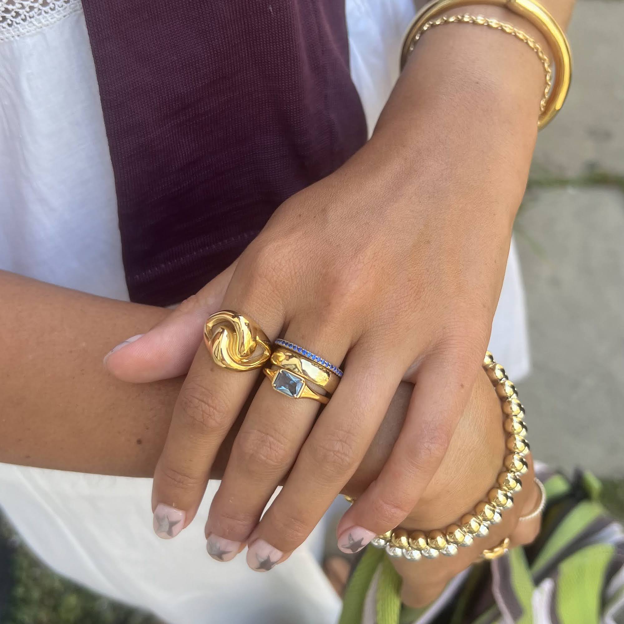 Close-up of a hand wearing gold rings and bracelets with a blurred background - seolgold