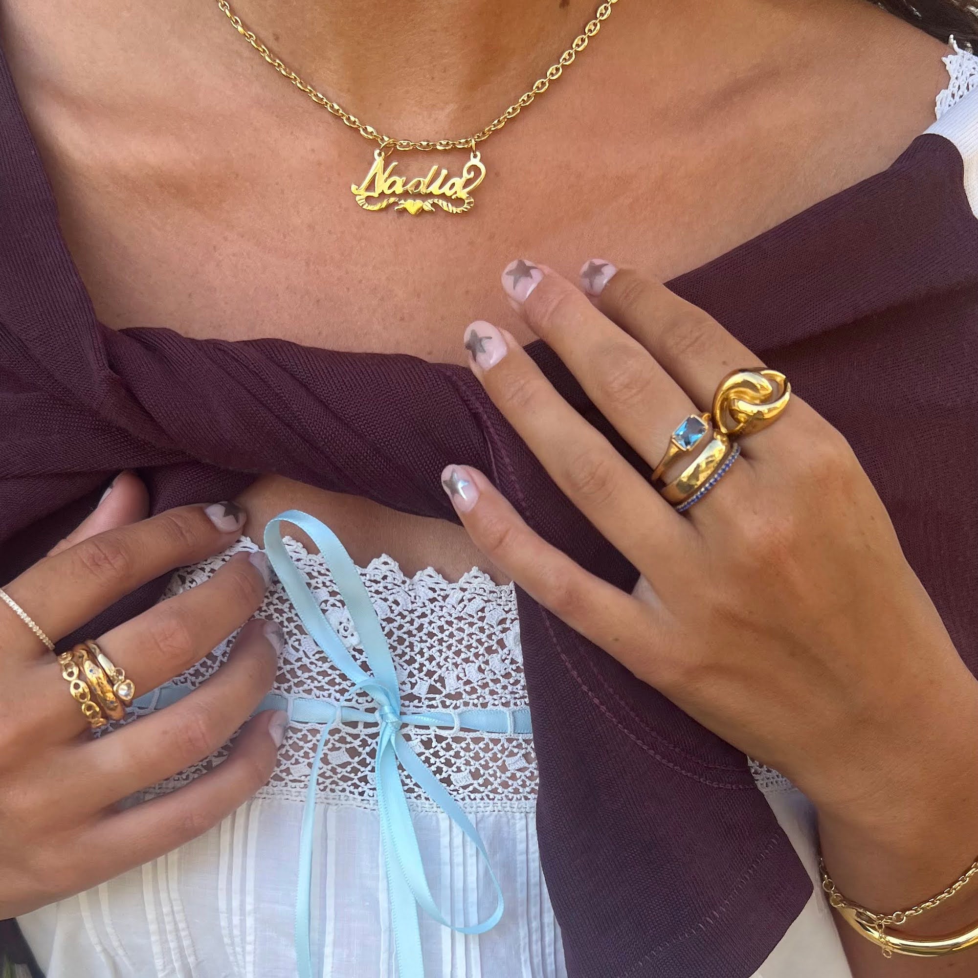 Close-up of a person wearing gold jewelry including a necklace, rings, and bracelets.
