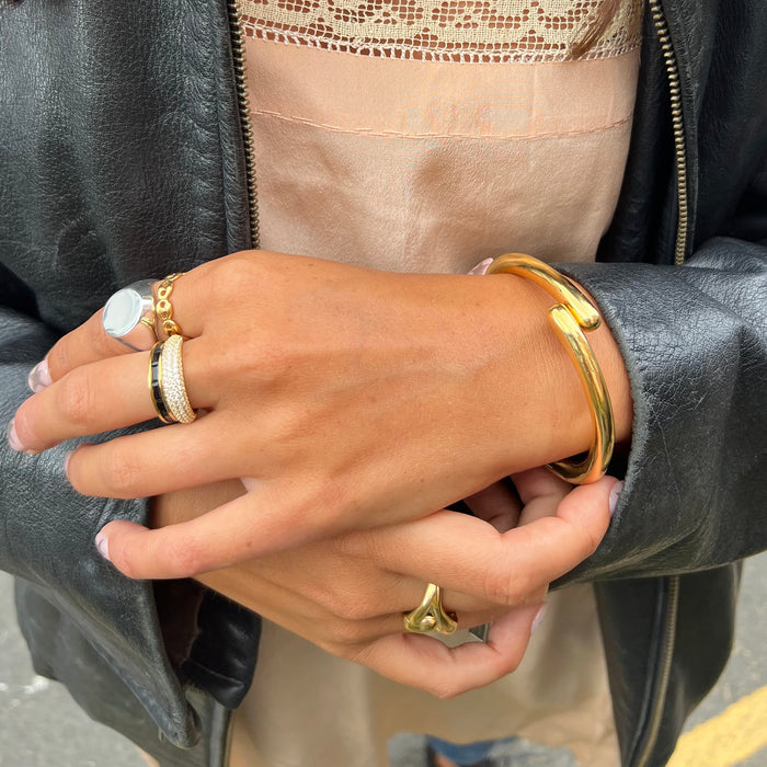 Close-up of a hand wearing gold rings and bracelets with a blurred background - hinged bangle - bypass bangle - seolgold