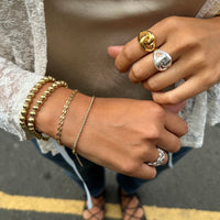 Close-up of hands wearing gold bracelets and rings on a blurred background - seolgold