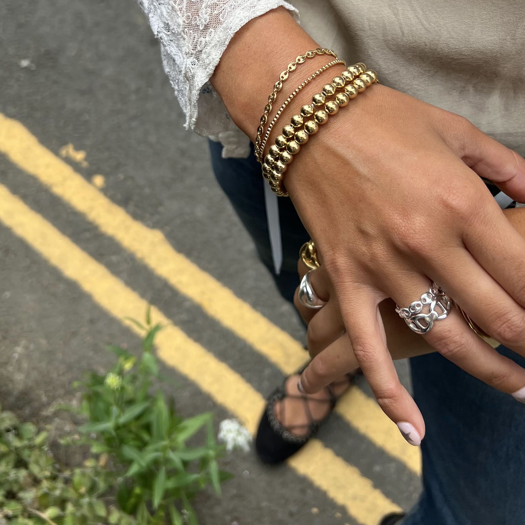 Close-up of a hand wearing gold bracelets and rings on a street with yellow lines - seol gold