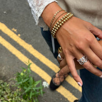Close-up of a hand wearing gold bracelets and rings on a street with yellow lines - seol gold