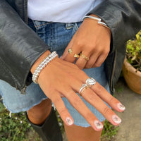 Close-up of hands with multiple rings and bracelets, wearing a black leather jacket and denim jeans - seolgold