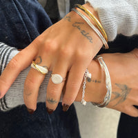 Close-up of a hand wearing multiple rings and bracelets with tattoos visible on the skin - seolgold