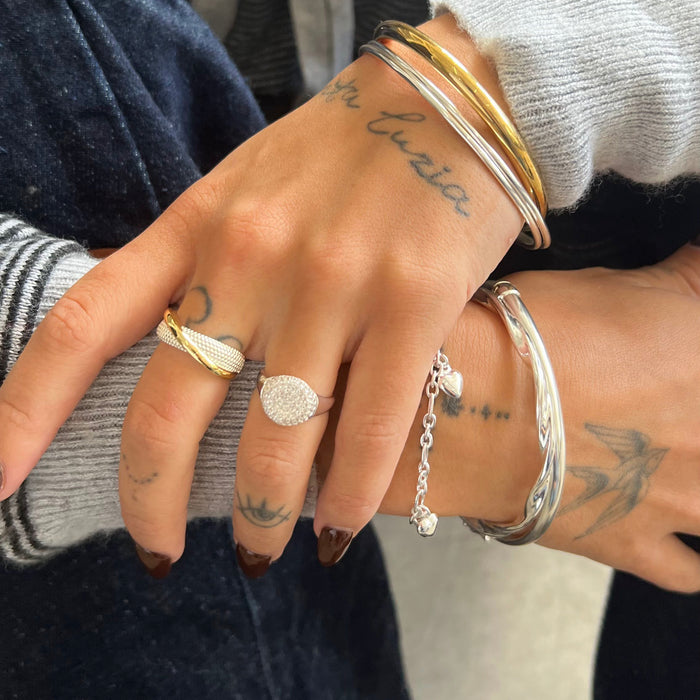 Close-up of a hand wearing multiple rings and bracelets with tattoos visible on the skin - seolgold