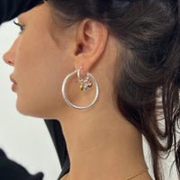 Close-up of a woman wearing silver hoop earrings with small charms - Seol Gold