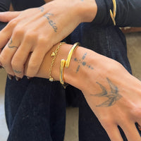 Close-up of hands wearing gold bracelets with tattoos on the skin - Seol Gold