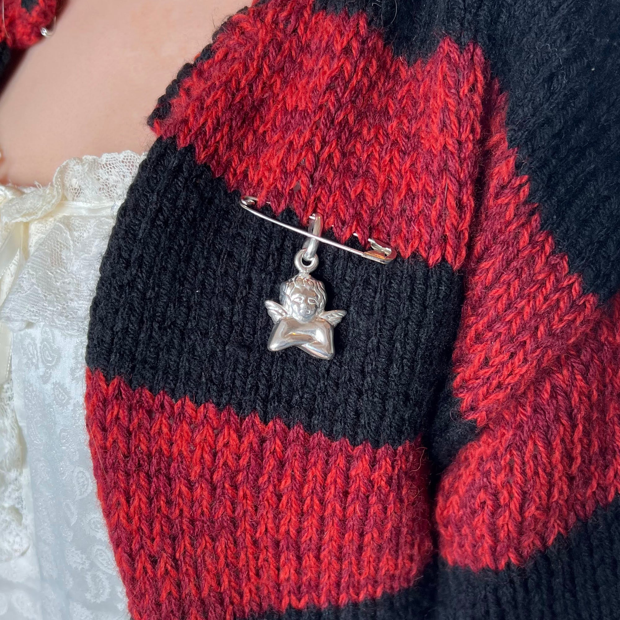 Close-up of a red and black knitted sweater with a silver angel brooch - seolgold