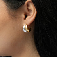 Close-up of an ear wearing a gold and silver earring with dark hair in the background - seolgold