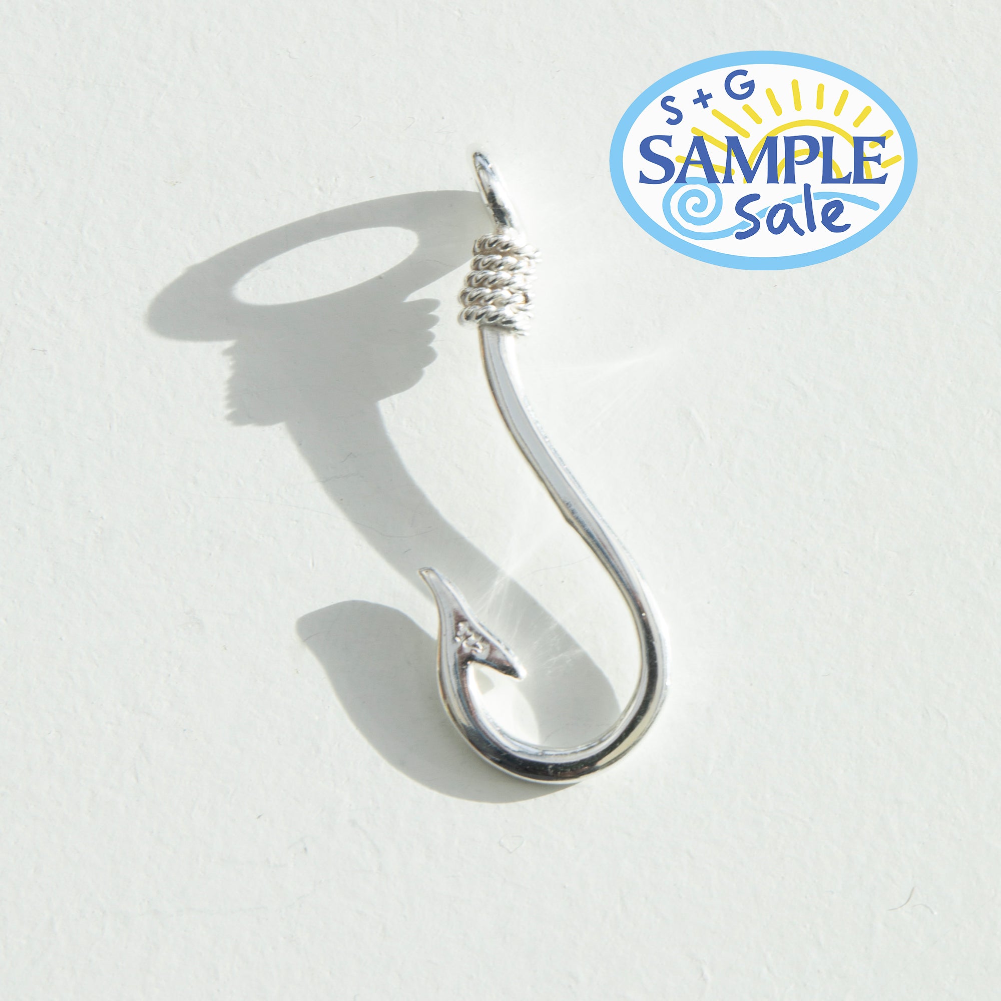 Silver fishing hook on a white background, featuring S+G Sample Sale logo - seolgold