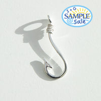 Silver fishing hook on a white background, featuring S+G Sample Sale logo - seolgold