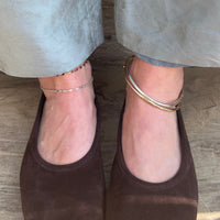 Brown suede shoes worn with light gray pants on a wooden floor wearing silver and gold anklets - seolgold