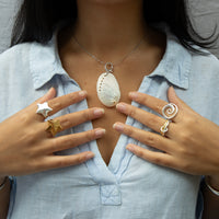 Person wearing a necklace with a large pendant, surrounded by multiple rings on fingers - seolgold