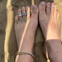 Feet with multiple toe rings and a bracelet on sand - seolgold