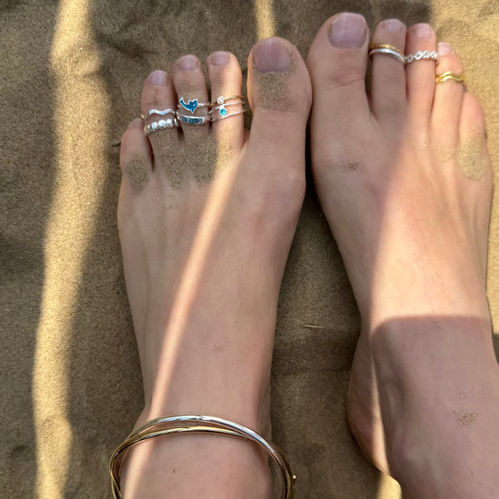 Feet with multiple toe rings and a bracelet on sand - seolgold