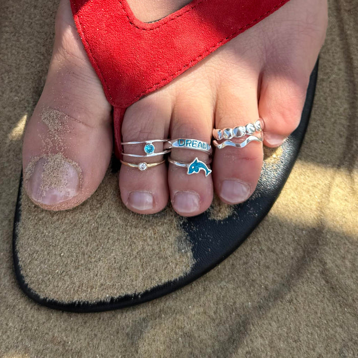 Close-up of toes with multiple rings on a sandal in the sand - seolgold