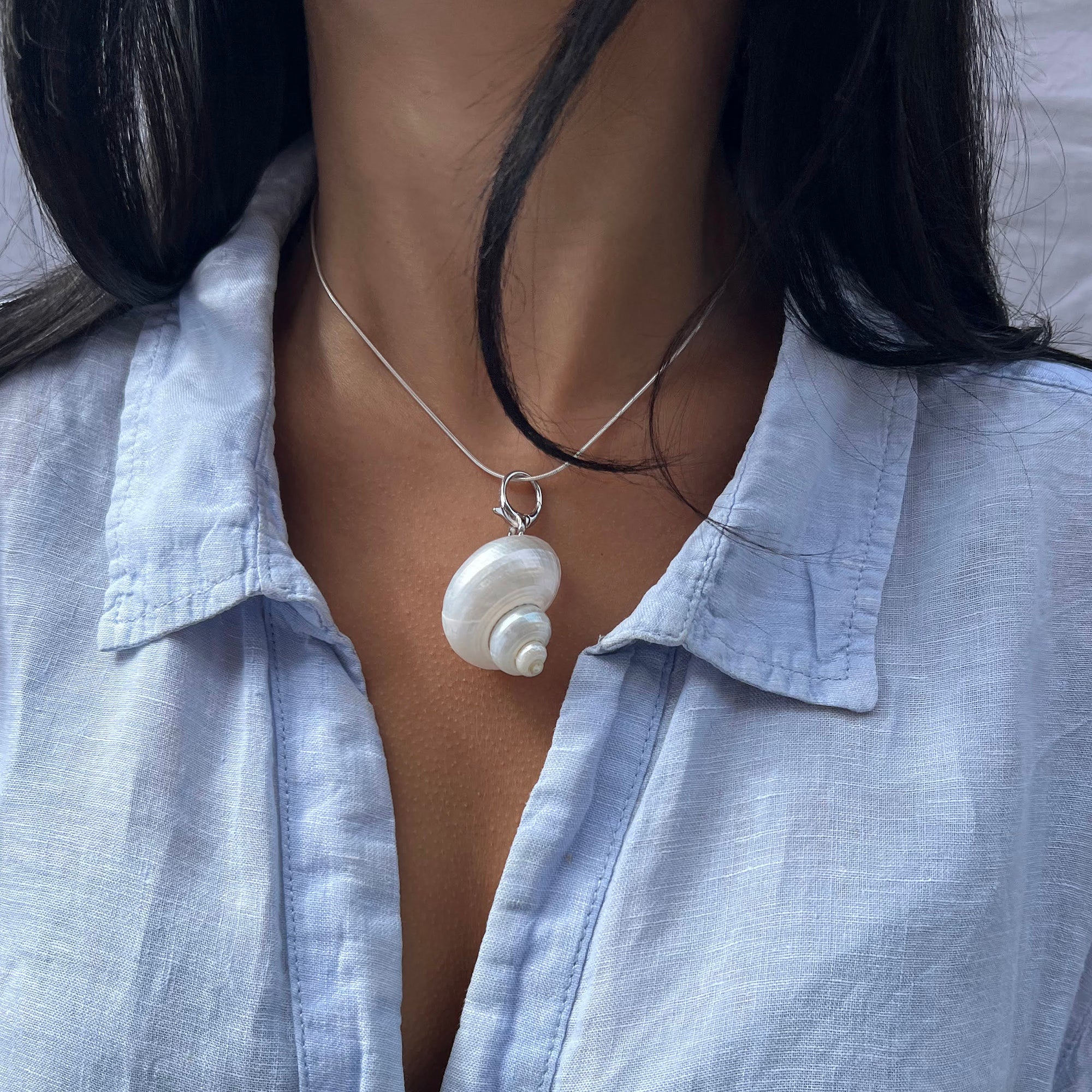 Person wearing a light blue shirt with a necklace featuring a shell pendant - seolgold