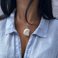 Person wearing a light blue shirt with a necklace featuring a shell pendant - seolgold