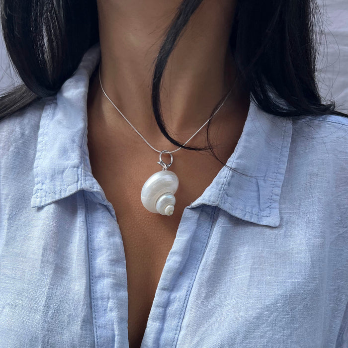 Person wearing a light blue shirt with a necklace featuring a shell pendant - seolgold