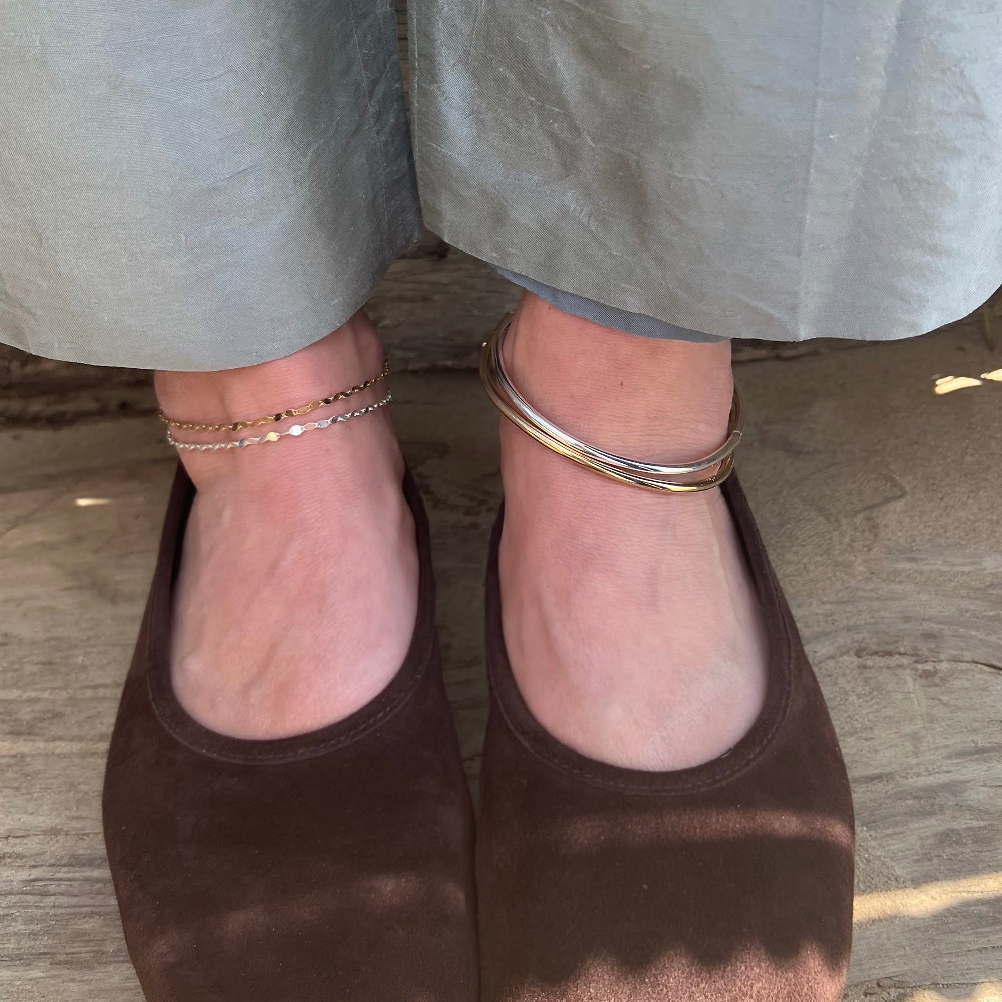 Brown shoes worn with light gray pants on a wooden floor wearing anklets - seolgold