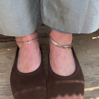 Brown shoes worn with light gray pants on a wooden floor wearing anklets - seolgold