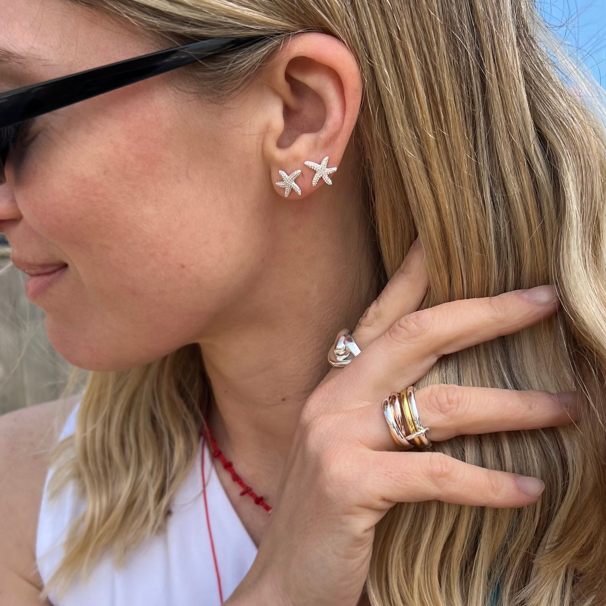 Close-up of a woman wearing silver starfish-shaped earrings and multiple rings - seolgold