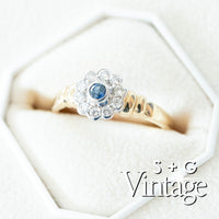 Gold ring with a blue gemstone and diamond accents on a white hexagonal stand, branded 'S + G Vintage' - seolgold