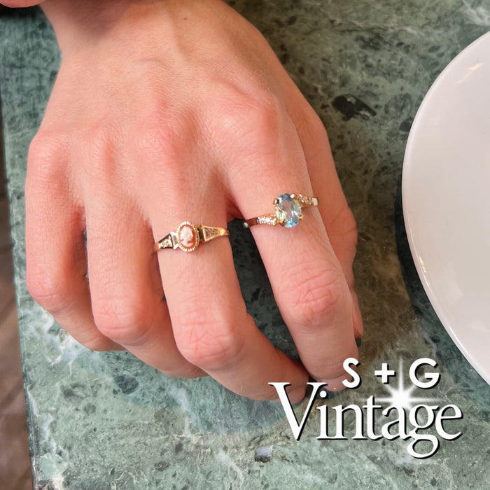 Gold ring with a blue gemstone and diamonds worn on a hand resting on a table, featuring 'S + G Vintage' branding - seolgold