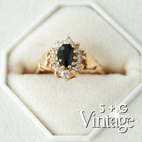 Gold ring with a black gemstone and diamonds on a white hexagonal stand, branded 'S + G Vintage' - seolgold