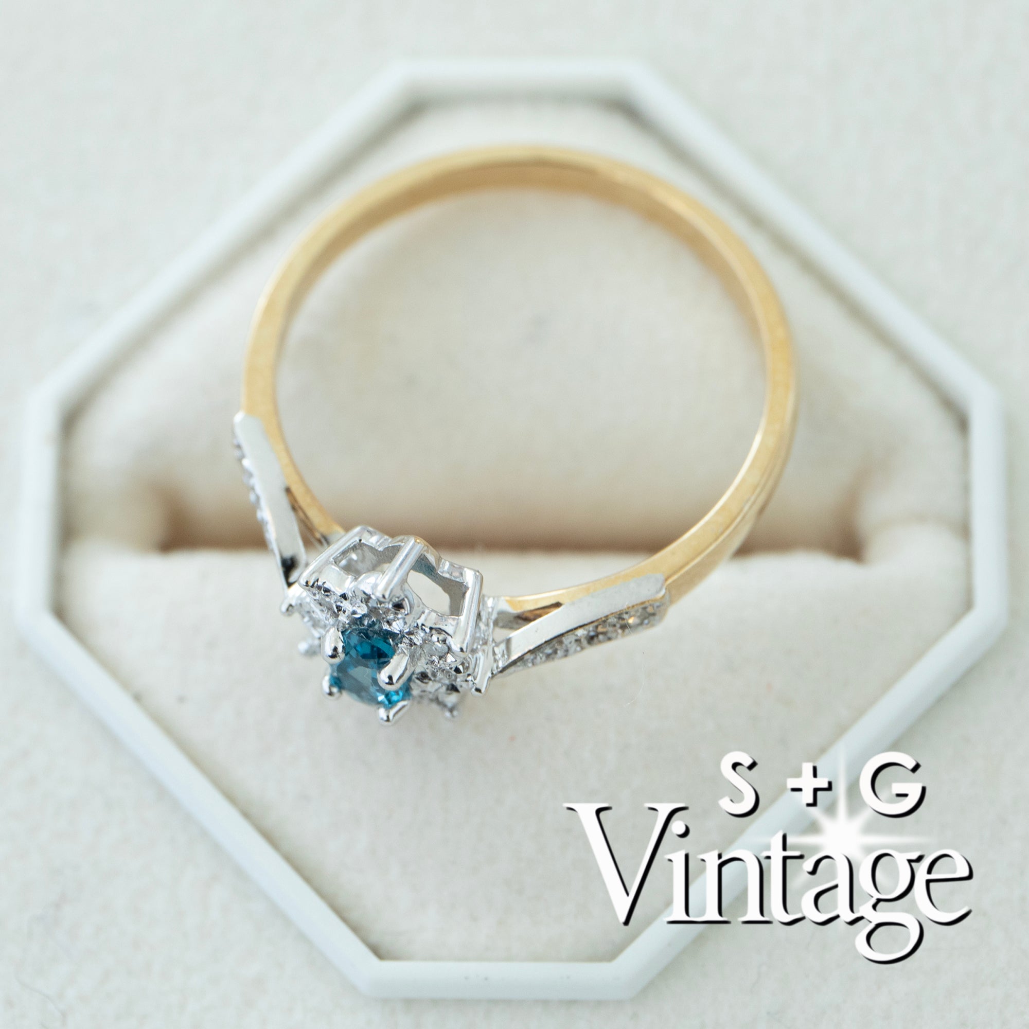 Gold ring with a blue gemstone on a white hexagonal stand, branded 'S + G Vintage' - seolgold
