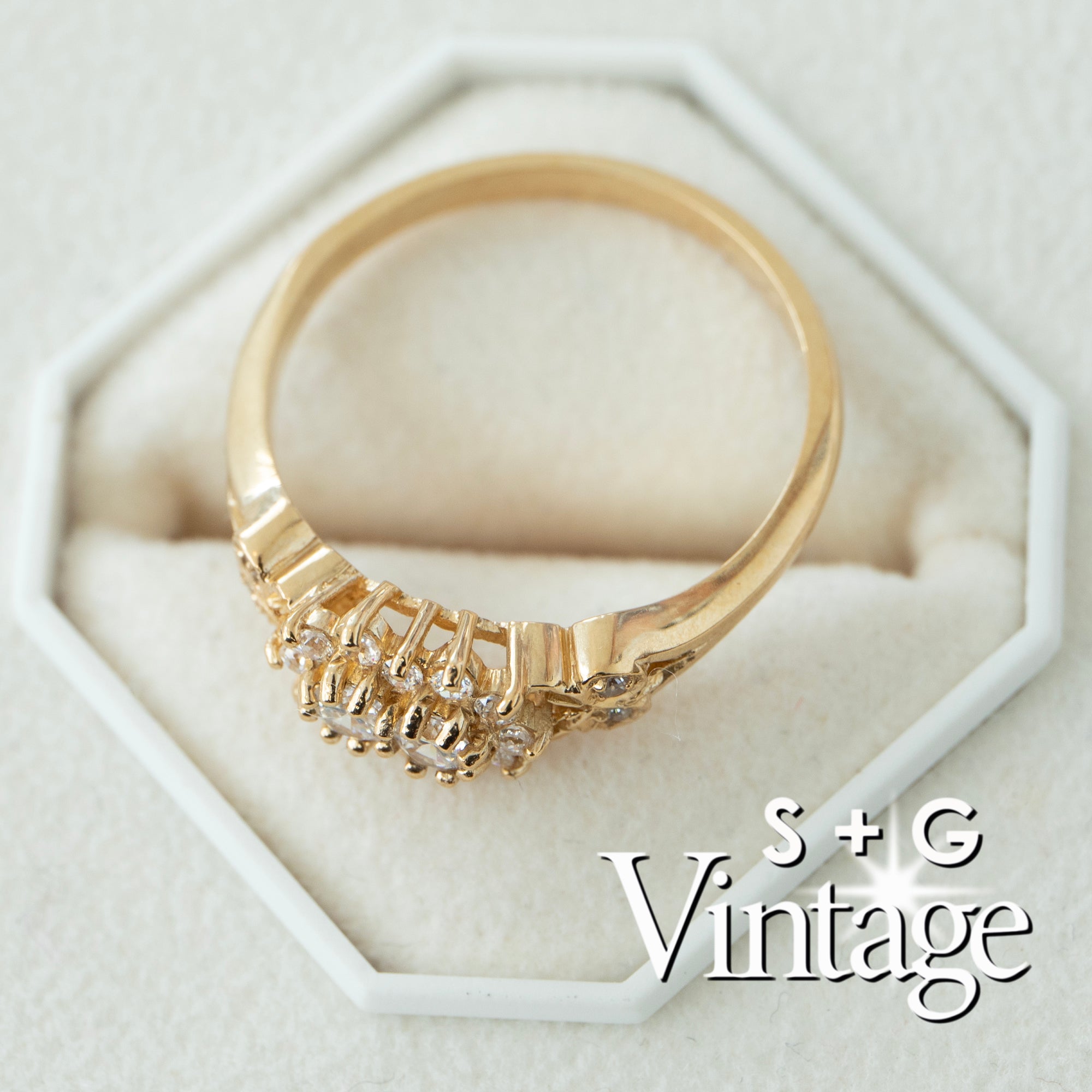 Gold ring with intricate design on a white hexagonal stand, featuring 'S + G Vintage' branding - seolgold