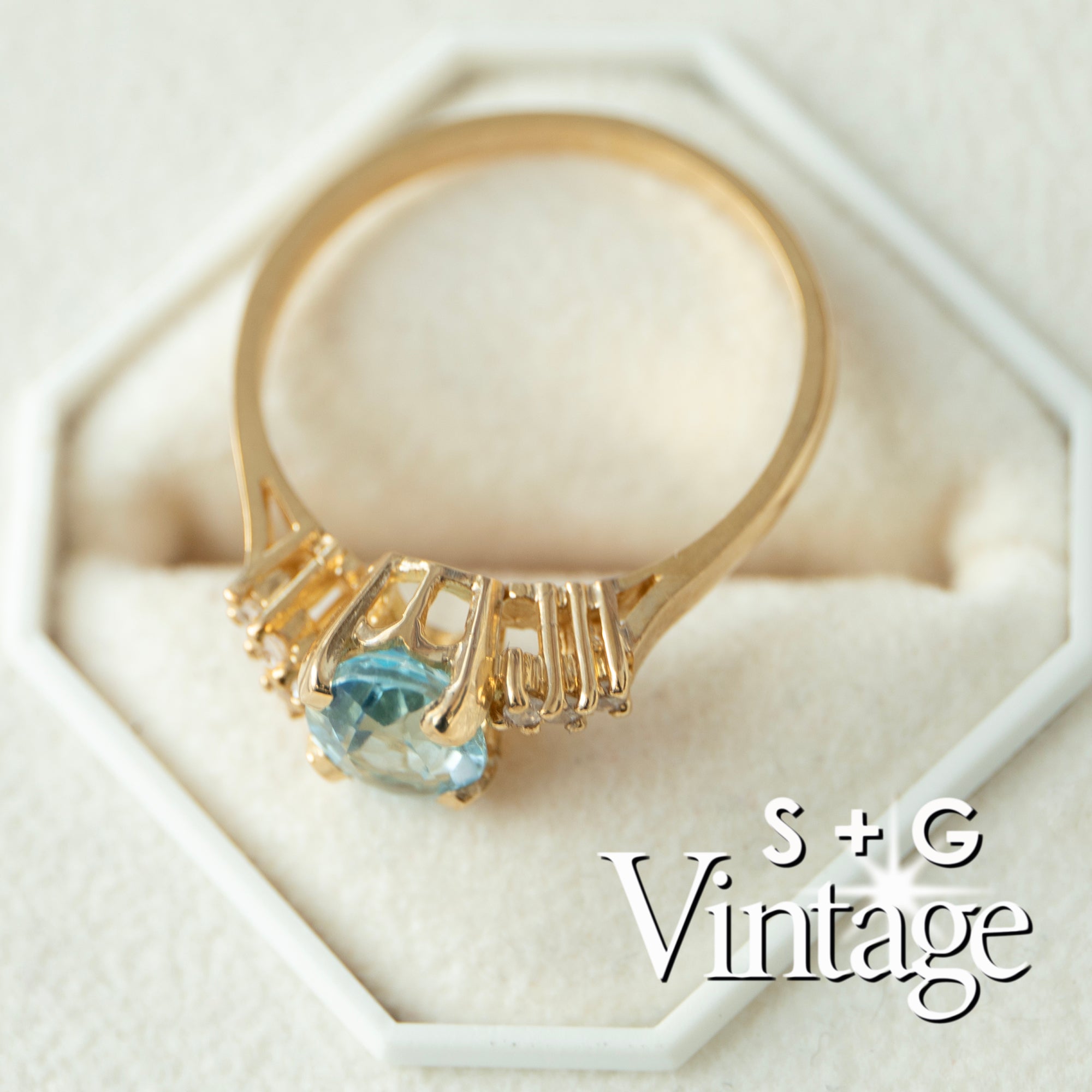 Gold ring with a blue gemstone on a white hexagonal stand, branded 'S + G Vintage' - seolgold