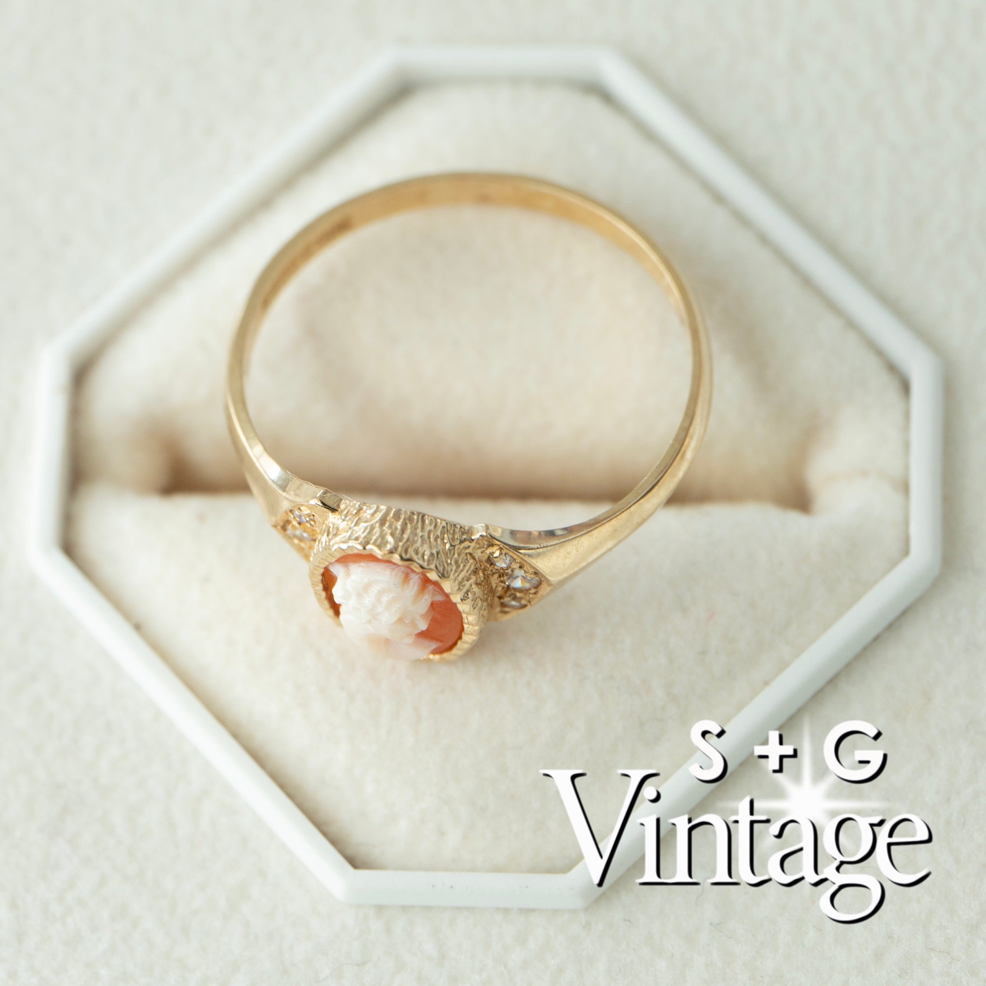 Gold ring with a cameo design on a white hexagonal stand, branded 'S + G Vintage' - seolgold