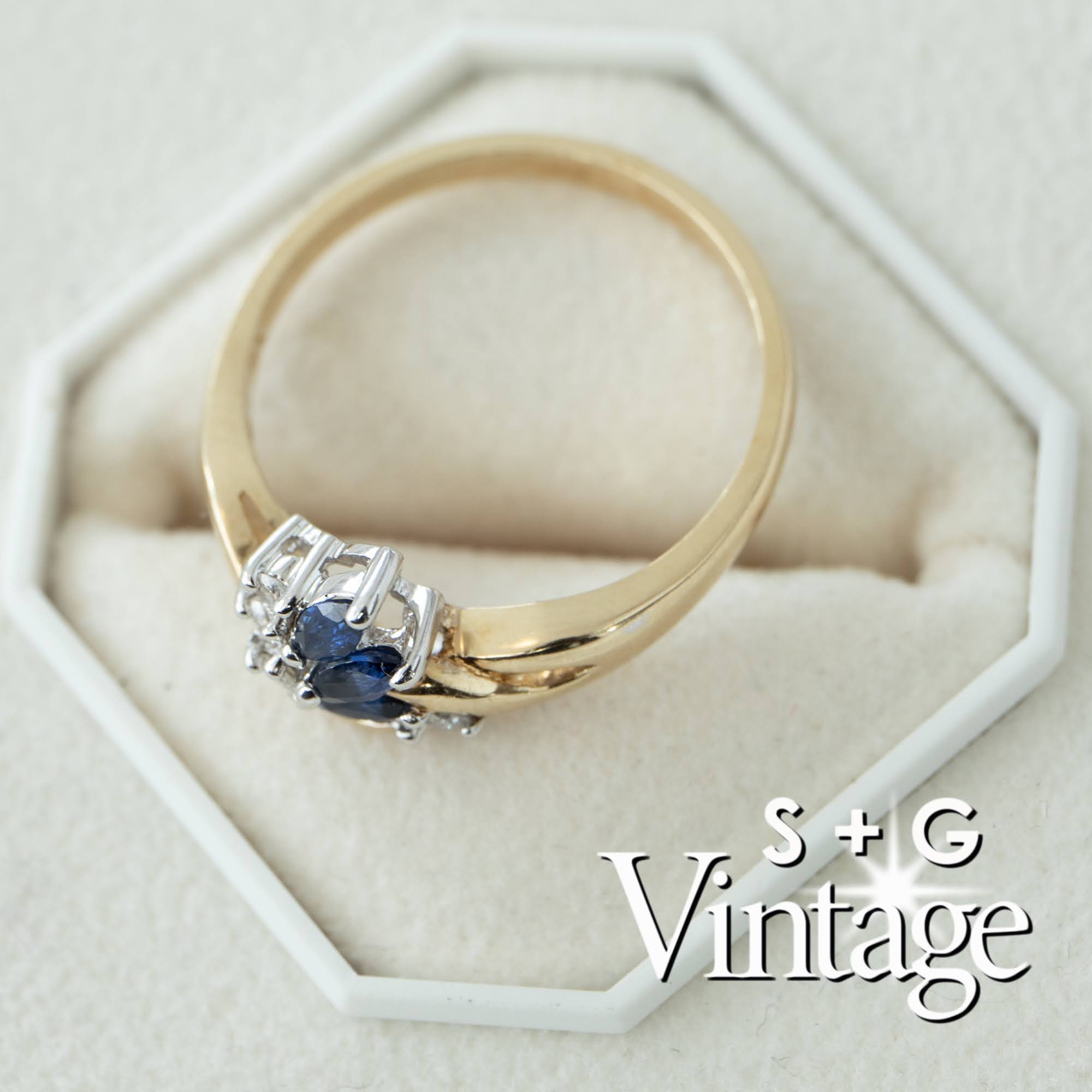 Gold ring with a blue gemstone on a white hexagonal stand, featuring 'S + G Vintage' branding - seolgold
