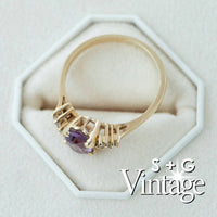 Gold ring with a purple gemstone on a white hexagonal stand with 'S + G Vintage' branding - seolgold